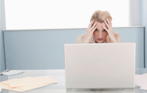 Woman sits in front of computer holding her head in her hands