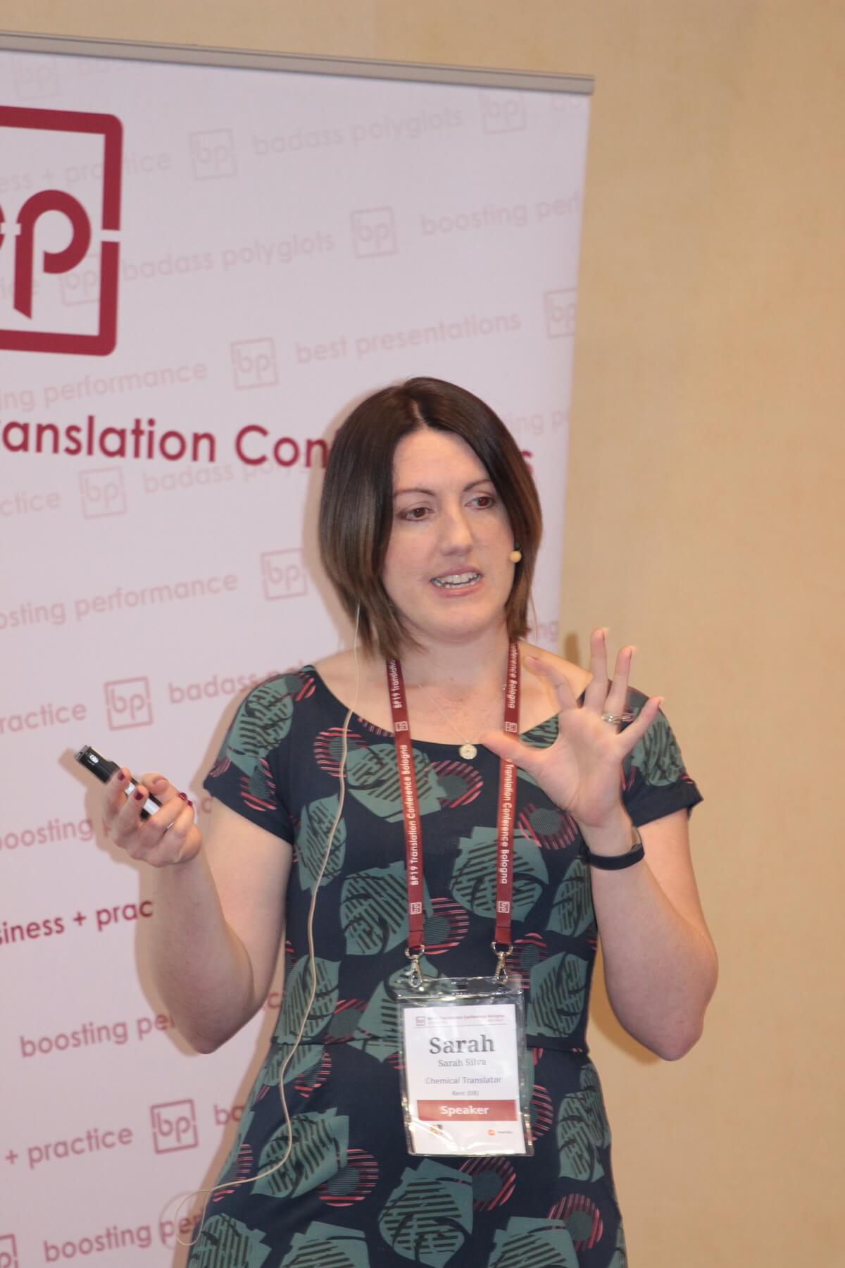 Sarah Silva standing in front of a banner, presenting at BP Translation Conference May 2019